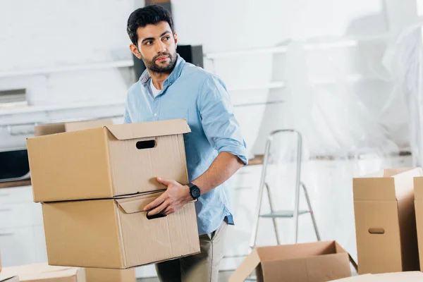 Beau latin homme tenant des boîtes tout en déménageant dans une nouvelle maison — Photo de stock