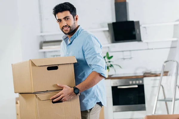 Allegro uomo latino che tiene scatole mentre si trasferisce in una nuova casa — Foto stock