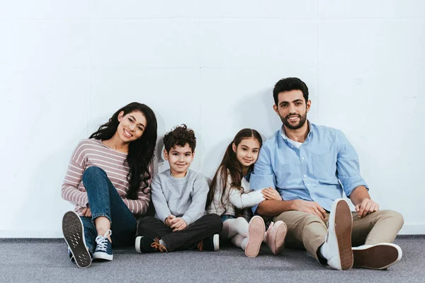 Cheerful hispanic family smiling while sitting on floor near white wall — Stock Photo