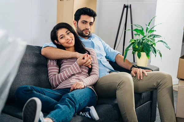 Glücklich lateinische Frau liegt auf Sofa neben Ehemann und Händchen haltend in neuem Zuhause — Stockfoto