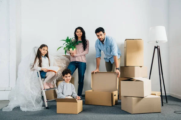 Cheerful latin family standing near boxes while moving into new home — Stock Photo