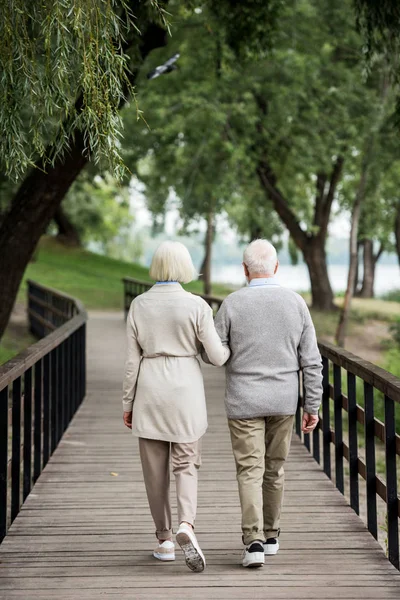 Pareja de ancianos caminando por el puente de madera en el parque - foto de stock