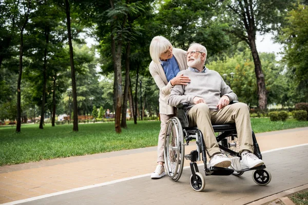 Nice senior woman with husband in wheelchair in park — Stock Photo