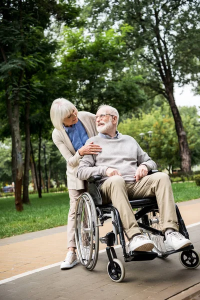 Mulher sênior agradável com marido em cadeira de rodas no parque — Fotografia de Stock