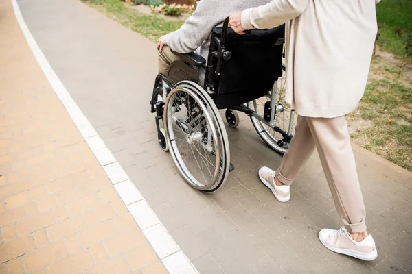 Vista recortada de mujer mayor con marido en silla de ruedas - foto de stock