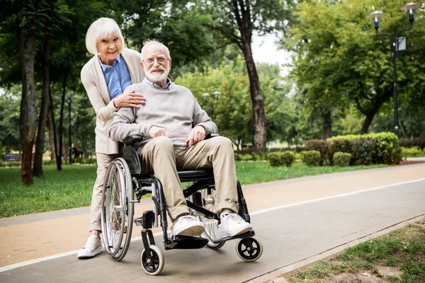 Happy senior couple, smiling woman with husband in wheelchair in park — Stock Photo