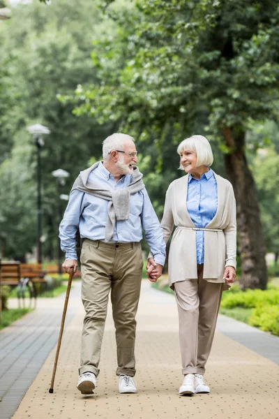 Smiling senior couple talking while walking in park — Stock Photo