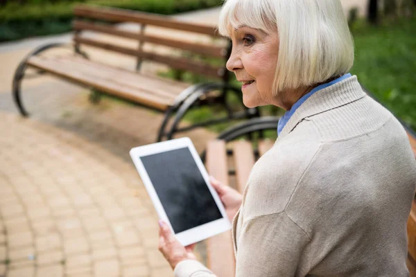 Вибірковий фокус старшої жінки, використовуючи цифровий планшет, сидячи на дерев'яній лавці — стокове фото