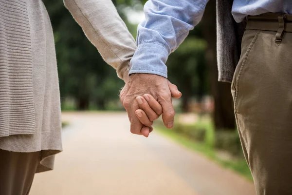 Vue recadrée du couple de personnes âgées tenant la main tout en marchant dans le parc — Photo de stock