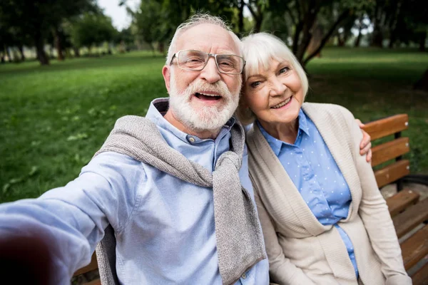 Selektiver Fokus eines fröhlich lächelnden Seniorenpaares auf Holzbank im Park — Stockfoto