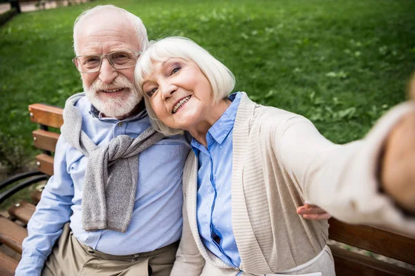 Foyer sélectif de heureux couple de personnes âgées assis sur un banc en bois dans le parc — Photo de stock