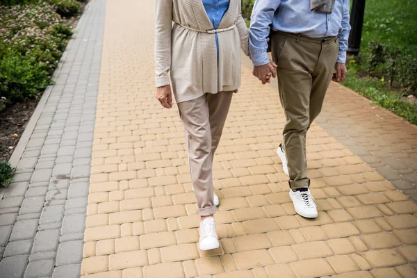 Vue partielle du couple de personnes âgées marchant sur le trottoir pavé du parc — Photo de stock