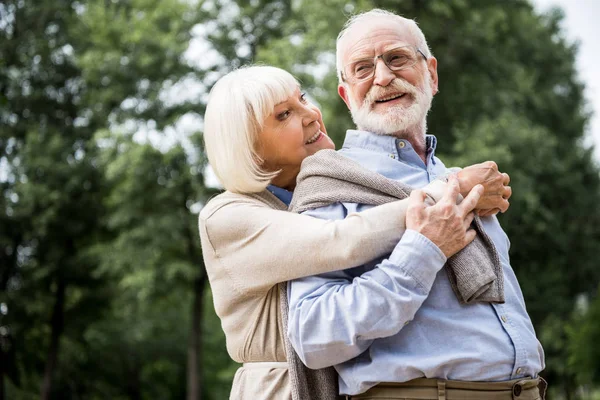 Felice coppia anziana che abbraccia e sorride nel parco — Foto stock