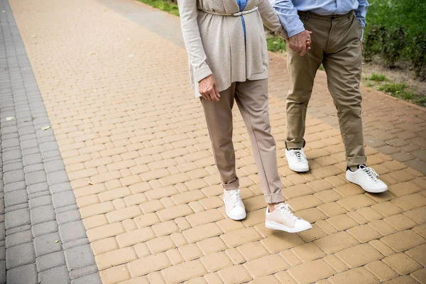 Обрезанный вид пожилой пары, идущей по асфальтированному тротуару в парке — стоковое фото