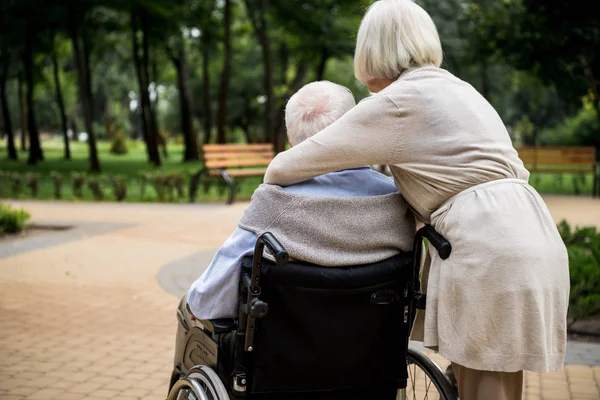 Back view of senior woman with husband in wheelchair in park — Stock Photo