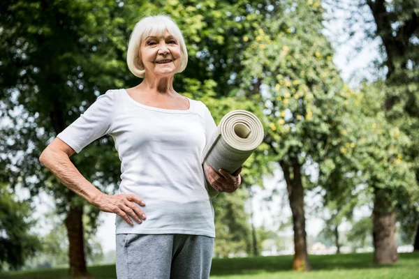 Felice donna anziana con tappetino fitness che tiene la mano sull'anca — Foto stock