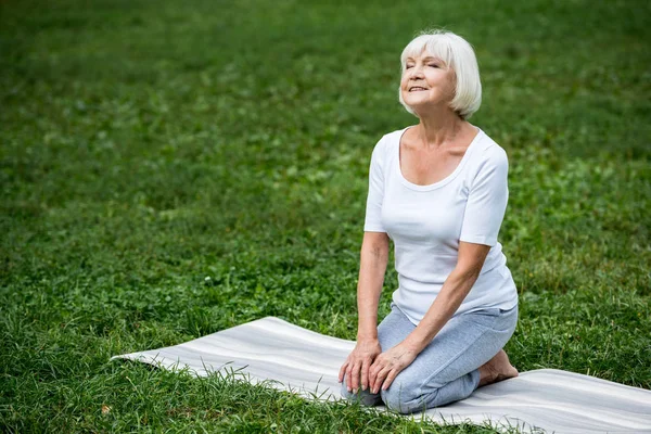 Heureuse femme âgée assise dans la pose de méditation avec les mains sur les genoux et les yeux fermés — Photo de stock