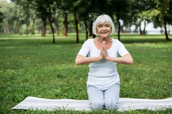 Старша жінка на йога мат в медитації Сухасана сидить позу зі складеними руками — стокове фото