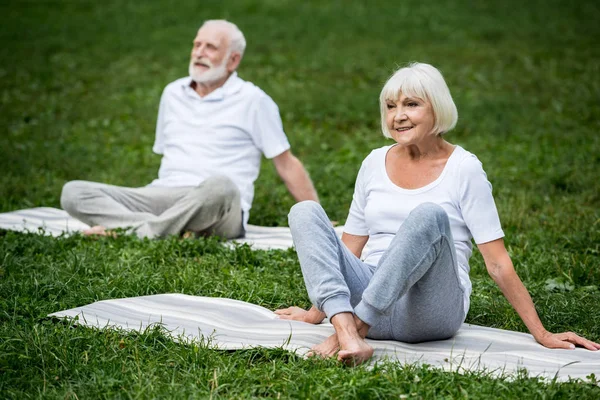 Casal sênior meditando em poses de relaxamento enquanto sentado em tapetes de ioga — Fotografia de Stock