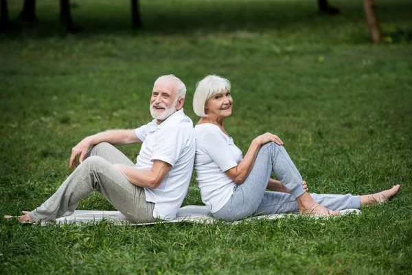 Happy senior couple resting on yoga mats on green lawn in park — Stock Photo