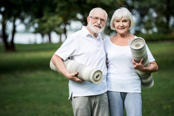 Улыбающаяся пожилая пара обнимается, держа в руках спортивные коврики — стоковое фото
