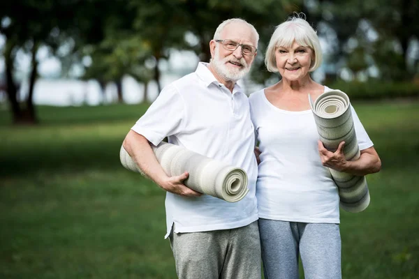 Sonriendo pareja mayor abrazando mientras sostiene alfombras de fitness - foto de stock