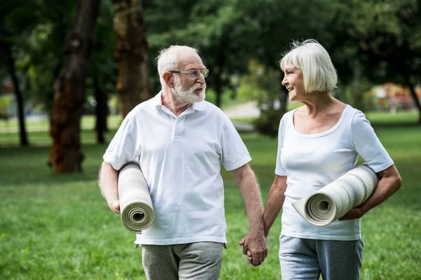 Feliz pareja de ancianos con colchonetas de fitness hablando mientras camina en el parque - foto de stock