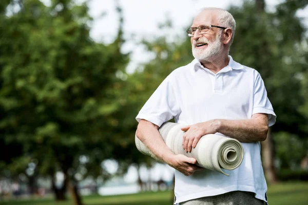 Felice uomo anziano con tappetino fitness nel parco — Foto stock