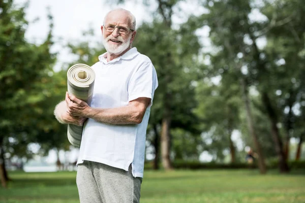 Happy senior man with fitness mat in park — Stock Photo
