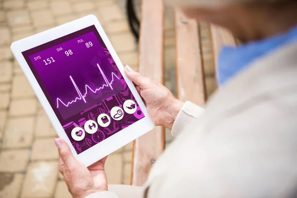 Selective focus of senior woman holding digital tablet with heartbeat rate on screen — Stock Photo