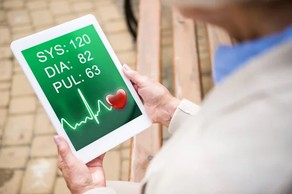 Selective focus of senior woman using digital table with heartbeat rate on screen — Stock Photo