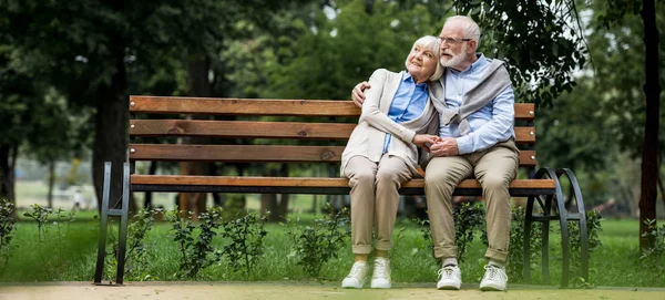 Felice coppia di anziani che si abbraccia mentre si siede su una panchina di legno nel parco — Foto stock