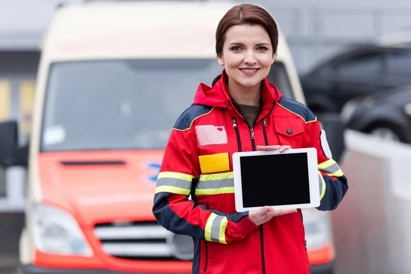 Paramédico sorridente em vermelho uniforme segurando comprimido digital com tela em branco — Fotografia de Stock