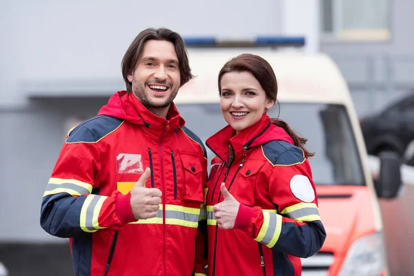 Lachende Sanitäter in roter Uniform zeigen Daumen hoch — Stockfoto