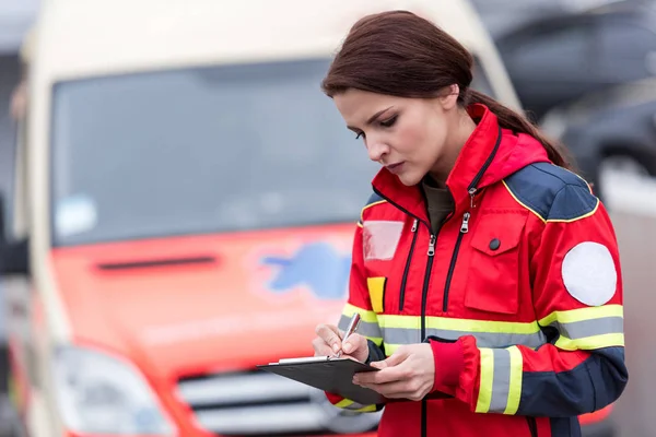 Concetrated femme ambulancier en uniforme écriture dans le presse-papiers — Photo de stock