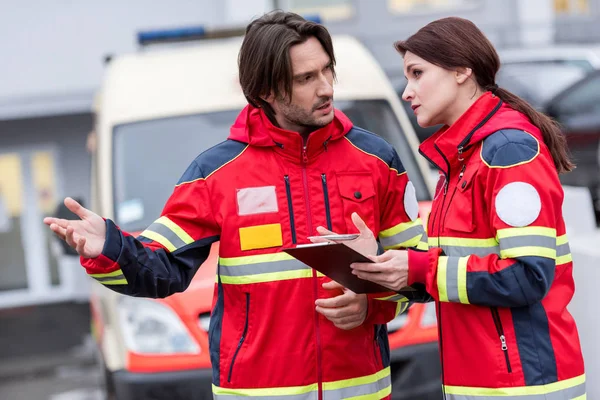 Paramédicos en uniforme rojo con portapapeles hablando en la calle - foto de stock