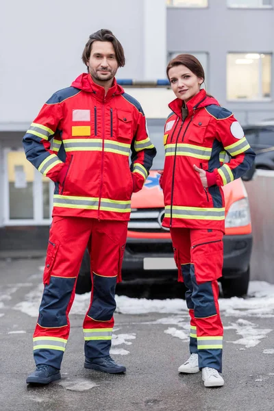 Visão de comprimento total de paramédicos em uniforme vermelho de pé com as mãos nos bolsos — Fotografia de Stock