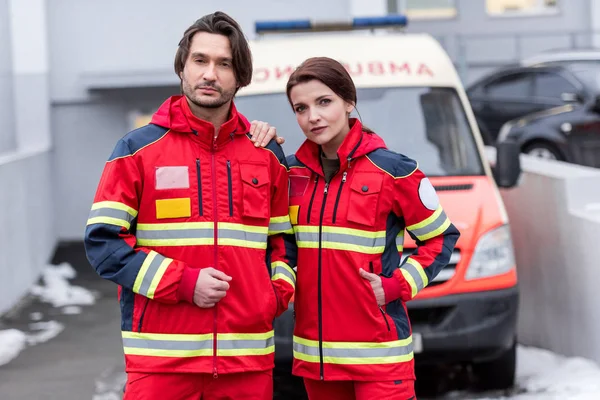 Paramédicos cansados en uniforme rojo de pie frente al coche ambulancia - foto de stock