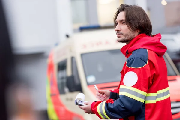 Ambulancier paramédical pensif avec presse-papiers regardant loin sur la rue — Photo de stock