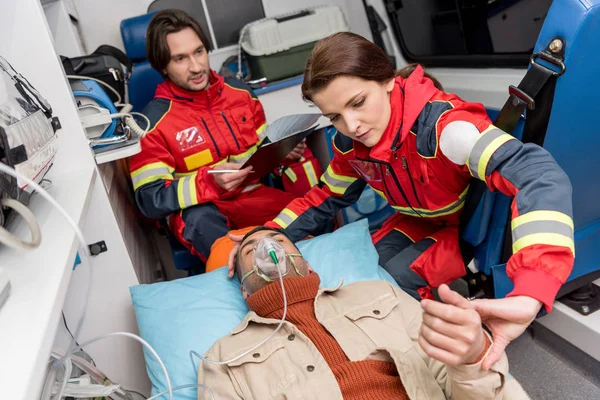 Paramedic holding oxygen mask on patient and checking pulse — Stock Photo