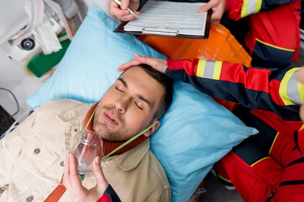 Cropped view of paramedic putting on oxygen mask on unconscious patient — Stock Photo
