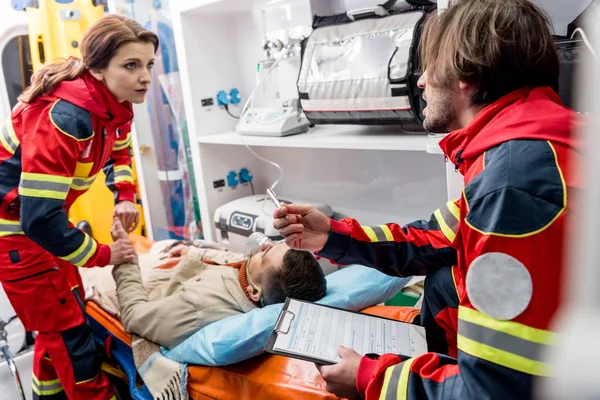 Paramédicos ayudando a hombre inconsciente en coche ambulancia - foto de stock