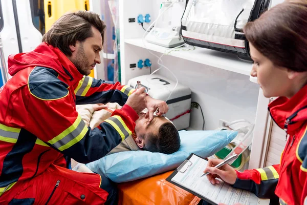 Paramedic doing eye examining in ambulance car — Stock Photo