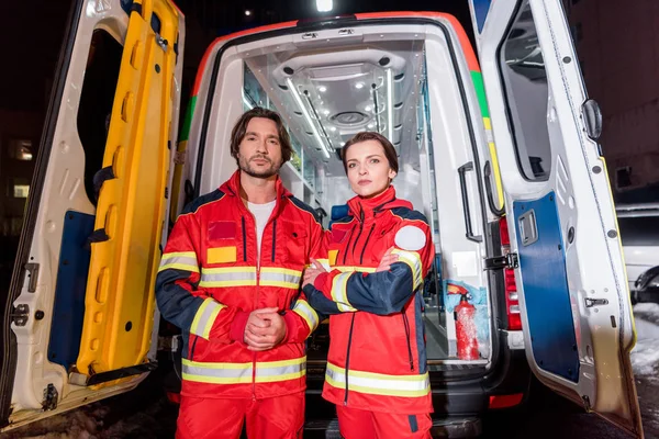 Paramédicos en uniforme rojo de pie frente al coche ambulancia - foto de stock