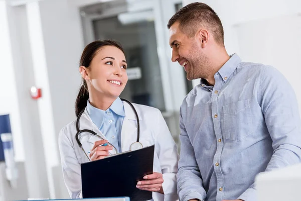 Smiling doctor talking to patient and writing in clipboard — Stock Photo