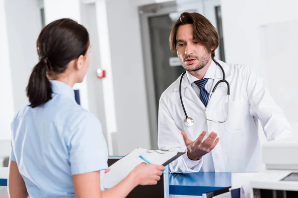 Guapo médico de bata blanca hablando con la enfermera - foto de stock