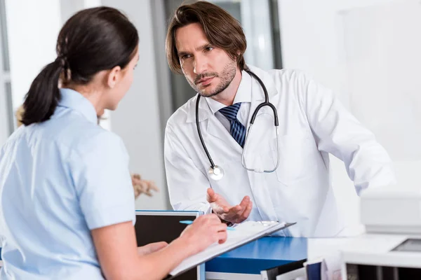 Médico sério com estetoscópio conversando com a enfermeira na clínica — Fotografia de Stock