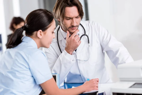 Médecin sérieux en manteau blanc parlant à l'infirmière à la clinique — Photo de stock