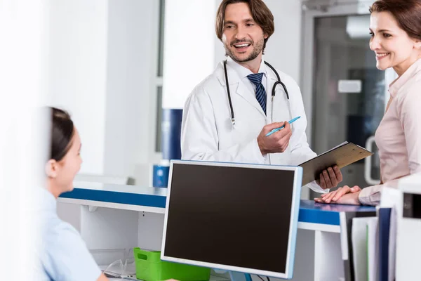 Médico sonriente hablando con enfermera y paciente en clínica - foto de stock