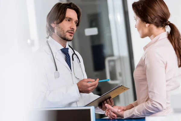 Médico com prancheta conversando com paciente na clínica — Fotografia de Stock